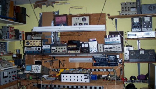 Photo of my workbench.  It has a shelf at about eye level above the work area.  The shelf is stacked 2 and sometimes 3 high with test equipment, most of it Heathkit.